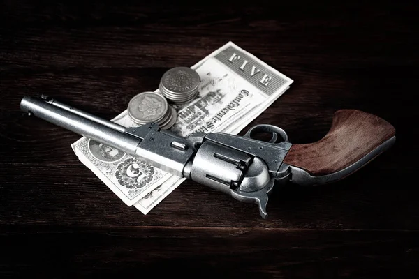 stock image Old west revolver with bill and silver dollars on wooden table