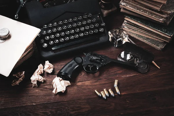 Vintage typewriter and revolver gun with ammunitions, books, blank paper, old ink pen pen on wooden table.