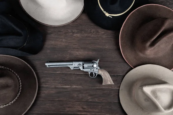 Gun with old west hats on wooden table. Top view.