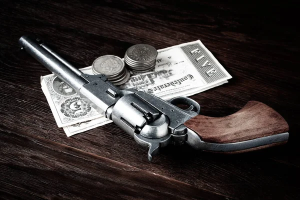Old west revolver with bill and silver dollars on wooden table