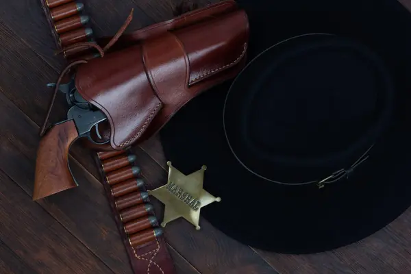 Marshal star with gun, holster and gun belt with old west black hat on table. Top view.