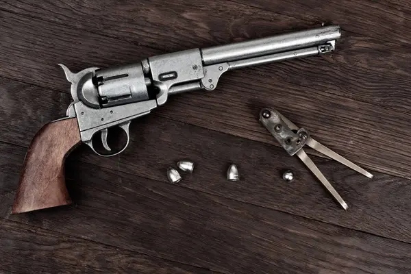 stock image Old West Revolver with bullet mold and bullets on wooden background.