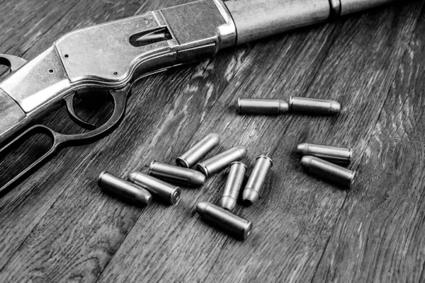 Old west rifle and ammunition on wooden table. Black and white.