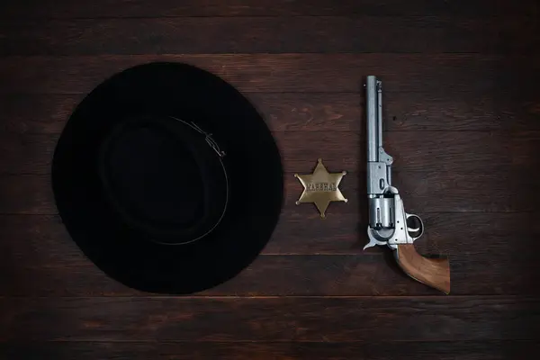 Old west gun, marshal star and black hat on table. Top view.