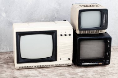 Old retro analog small TV sets stand on wooden floor front grey concrete wall background. clipart