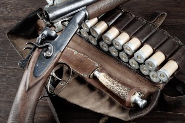 hunting double barreled side shotgun with cartridges in bandolier on wooden table. clipart