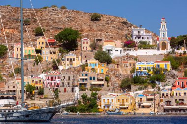 Sunny View of Ano Symi with colorful houses and Annunciation Church, Dodecanese islands, Greece clipart