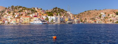 Sunny panorama of Ano Symi with colorful houses and Clocktower, Dodecanese islands, Greece clipart