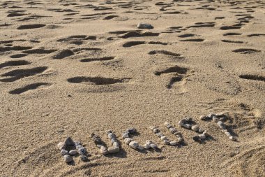 Ağustos ve yaz konsepti taşlarla dolu bir plajda yazılmış harflerle.