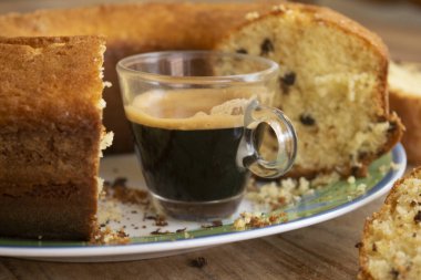 İki dilim çöreğin arasına bir fincan kahve ve arka plandaki bütün pasta.