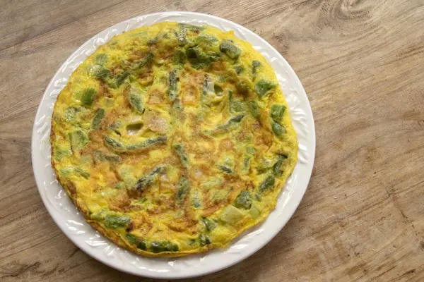 Yeşil kuşkonmaz ve parmesanlı ev yapımı omlet, kırsal ahşap bir masada beyaz bir tabakta. Arka planda beyaz kuşkonmaz. Sağlıklı kahvaltı ve kahvaltı için mükemmel..