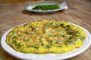 Yeşil kuşkonmaz ve parmesanlı ev yapımı omlet, kırsal ahşap bir masada beyaz bir tabakta. Arka planda beyaz kuşkonmaz. Sağlıklı kahvaltı ve kahvaltı için mükemmel..