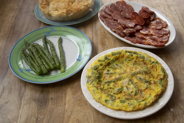 Taze yeşil kuşkonmazla dolu ev yapımı altın bir omletin yakın çekimi. Mükemmel pişirilmiş ve ahşap bir masada beyaz bir tabakta sunuluyor. Arka planda biraz daha kuşkonmaz var.
