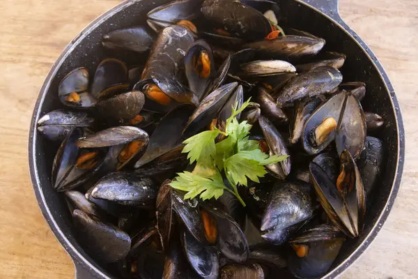 Taze maydanozla süslenmiş ve servis edilmeye hazır, koyu bir tencerede leziz, taze haşlanmış midyeler.