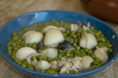 Geleneksel İtalyan deniz ürünleri, yumuşak mürekkep balığı ve yeşil bezelye ile, kırsal ahşap masada mavi bir kasede servis edilir.