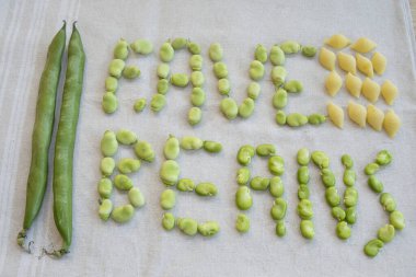 Yoğun yeşil fasulyeler, hem kabuklarında hem de kabuklarında, bahar pişirmek için taze malzemeler sergilenen kuru koni makarnasının yanında düzenlenir.