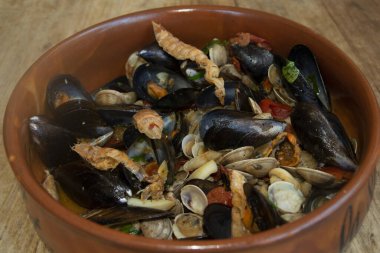 Lezzetli bir deniz ürünleri karışımı midye, istiridye ve karides ahşap bir masada servis edilen rustik kil kasesinde, gurme yemek için mükemmel.