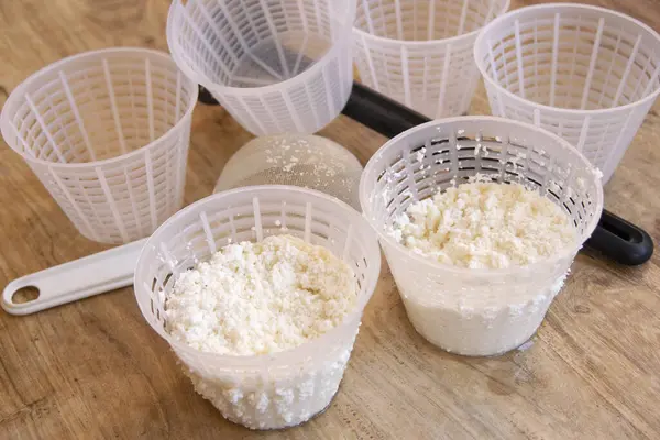 Tahta masadaki plastik sepetlerde süzen taze ricotta peyniri, elek ve küf şeklinde.