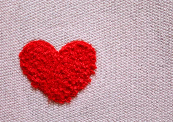 Yumuşak kırmızı kalp pembe kumaş arka planında iplikten örülmüş. Aşkın, sıcaklığın ve sevginin sembolü. Yakın plan, minimalist stil.