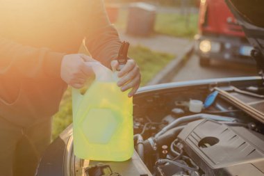 Açık kaputun altındaki araba deposuna cam temizleme sıvısı dökülüyor.