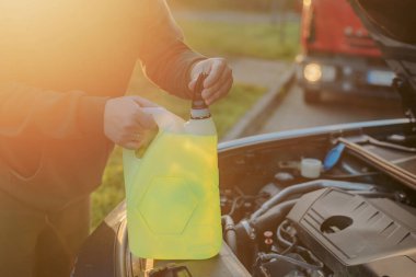 Açık kaputun altındaki araba deposuna cam temizleme sıvısı dökülüyor.