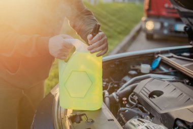 Açık kaputun altındaki araba deposuna cam temizleme sıvısı dökülüyor.