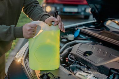 Açık kaputun altındaki araba deposuna cam temizleme sıvısı dökülüyor.