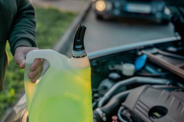 Açık kaputun altındaki araba deposuna cam temizleme sıvısı dökülüyor.