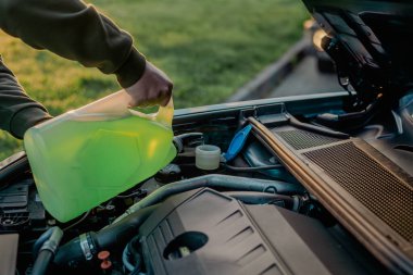 Açık kaputun altındaki araba deposuna cam temizleme sıvısı dökülüyor.