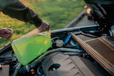 Açık kaputun altındaki araba deposuna cam temizleme sıvısı dökülüyor.