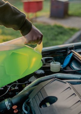 Açık kaputun altındaki araba deposuna cam temizleme sıvısı dökülüyor.