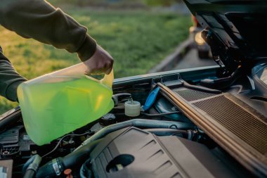 Açık kaputun altındaki araba deposuna cam temizleme sıvısı dökülüyor.