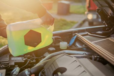 Açık kaputun altındaki araba deposuna cam temizleme sıvısı dökülüyor.