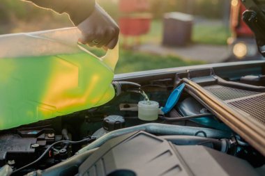 Açık kaputun altındaki araba deposuna cam temizleme sıvısı dökülüyor.