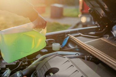 Açık kaputun altındaki araba deposuna cam temizleme sıvısı dökülüyor.