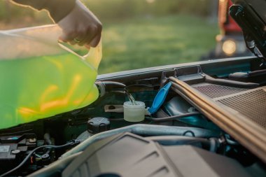 Açık kaputun altındaki araba deposuna cam temizleme sıvısı dökülüyor.