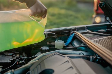 Açık kaputun altındaki araba deposuna cam temizleme sıvısı dökülüyor.