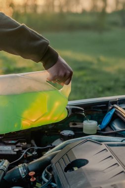 Açık kaputun altındaki araba deposuna cam temizleme sıvısı dökülüyor.