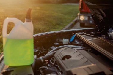 Açık kaputun altındaki araba deposuna cam temizleme sıvısı dökülüyor.