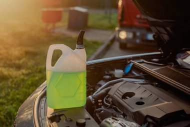 Açık kaputun altındaki araba deposuna cam temizleme sıvısı dökülüyor.