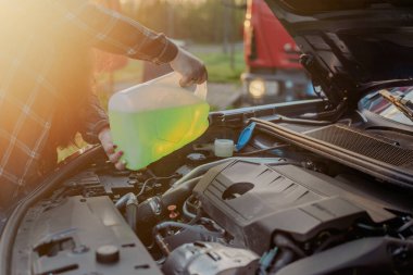 Açık kaputun altındaki araba deposuna cam temizleme sıvısı dökülüyor.