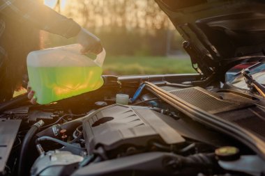 Açık kaputun altındaki araba deposuna cam temizleme sıvısı dökülüyor.