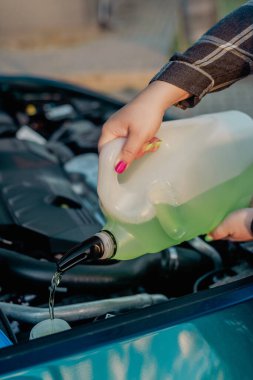 Açık kaputun altındaki araba deposuna cam temizleme sıvısı dökülüyor.