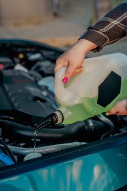 Açık kaputun altındaki araba deposuna cam temizleme sıvısı dökülüyor.