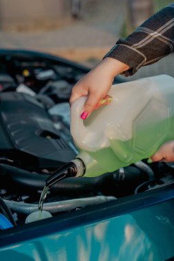 Açık kaputun altındaki araba deposuna cam temizleme sıvısı dökülüyor.