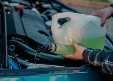 Açık kaputun altındaki araba deposuna cam temizleme sıvısı dökülüyor.