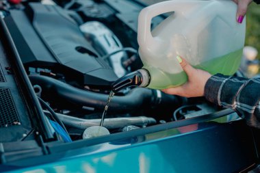 Açık kaputun altındaki araba deposuna cam temizleme sıvısı dökülüyor.