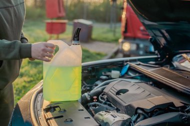 Açık kaputun altındaki araba deposuna cam temizleme sıvısı dökülüyor.