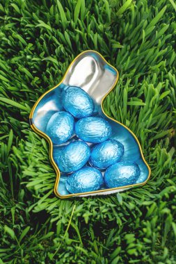 Yeşil çimlerin üzerinde mavi Paskalya yumurtalarıyla dolu tavşan şeklinde bir kap.