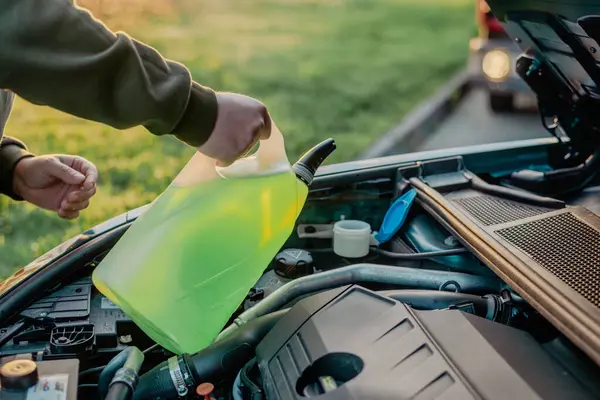 Açık kaputun altındaki araba deposuna cam temizleme sıvısı dökülüyor.